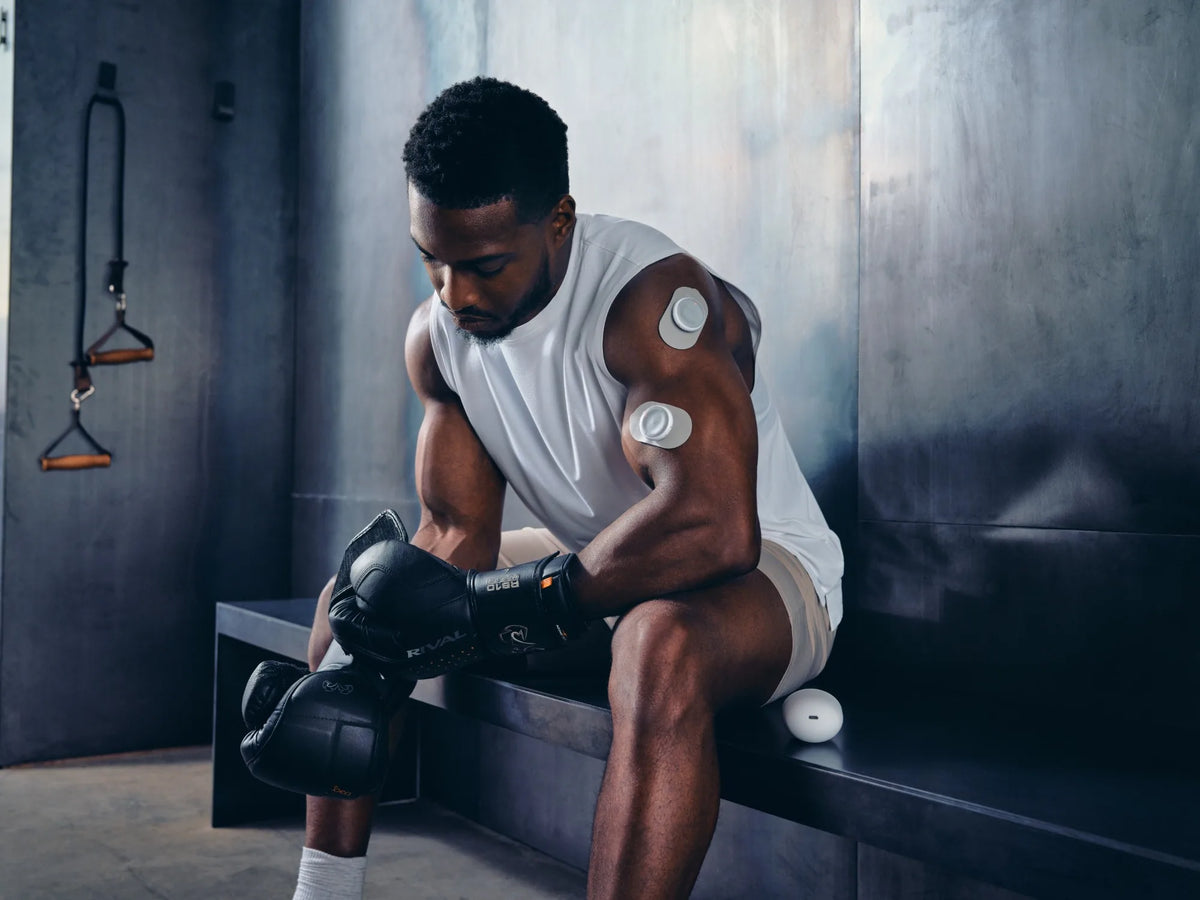Boxer resting on a gym bench with two Pulsio TENS Pods on his arm